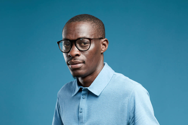 Muotokuva Afrikkalainen nuori mies yllään lasit ja sininen paita katselee kameraa sinisellä pohjalla
 - Valokuva, kuva