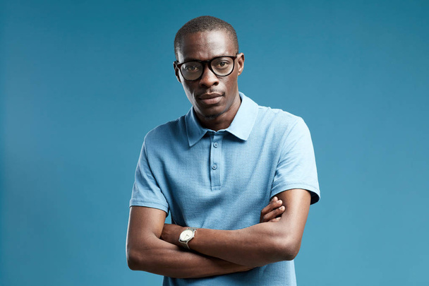 Portrait de jeune homme africain portant des lunettes et chemise bleue regardant la caméra sur fond bleu
 - Photo, image