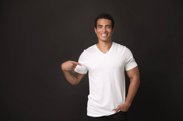 Handsome young African-American man in blank t-shirt on black background. Space for design - Foto, imagen