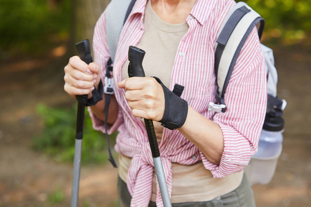 Close-up of mature woman holding canes and doing nordic walking in the forest - Photo, Image