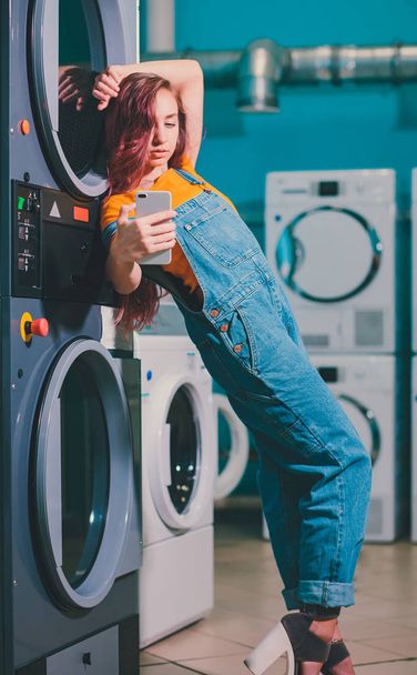 Young woman searching clothes in washing machine drum at laundromat. - Photo, Image