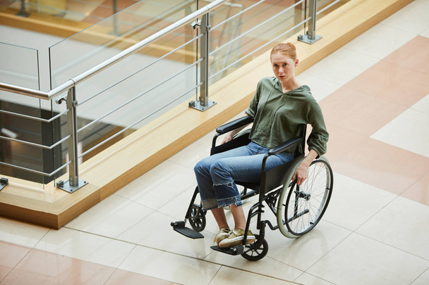 Joven mujer pelirroja sentada en silla de ruedas en un hospital moderno
 - Foto, Imagen