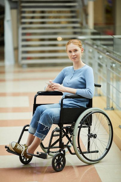 Joven mujer discapacitada sentada en silla de ruedas y leyendo el mensaje en el teléfono móvil
 - Foto, imagen