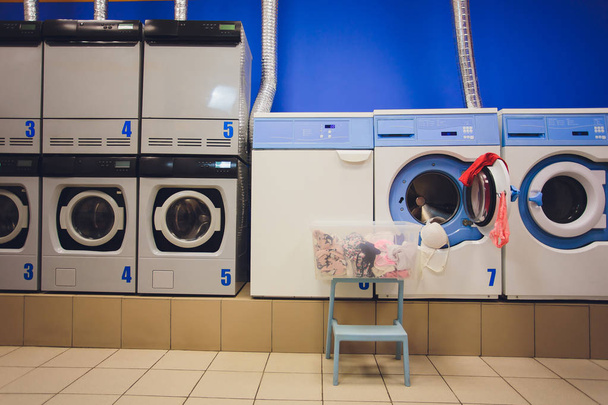 Self servis çamaşırhanede giysi dolu sepetli profesyonel çamaşır makineleri. - Fotoğraf, Görsel