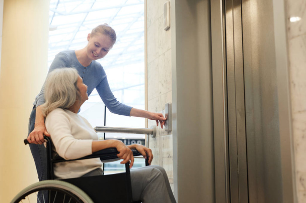Mujer joven ayudando a paciente discapacitado senior en silla de ruedas elevador móvil
 - Foto, imagen