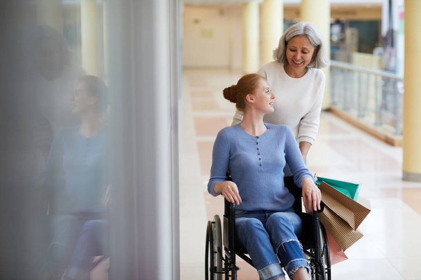Инвалидная женщина в инвалидном кресле ходит по магазинам со старшей матерью в торговом центре
 - Фото, изображение
