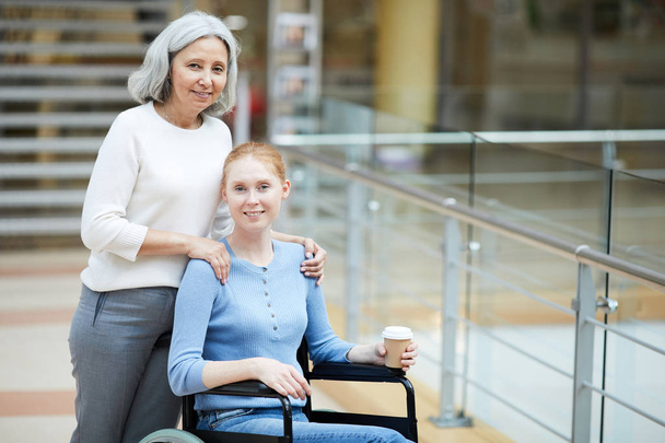 Zdravotně postižená mladá žena na invalidním vozíku chůze se starší matkou v nákupním centru - Fotografie, Obrázek