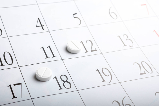 duas pílulas no calendário por mês. comprimidos brancos forma redonda em uma folha de calendário
 - Foto, Imagem