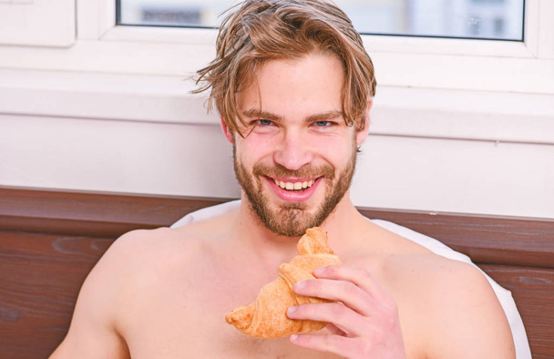 Man bearded handsome guy eating breakfast in bed. Handsome man drinking morning coffee in the bed. Handsome young man enjoying his morning cup of coffee laying in bed hotel room happy smiling. - Valokuva, kuva