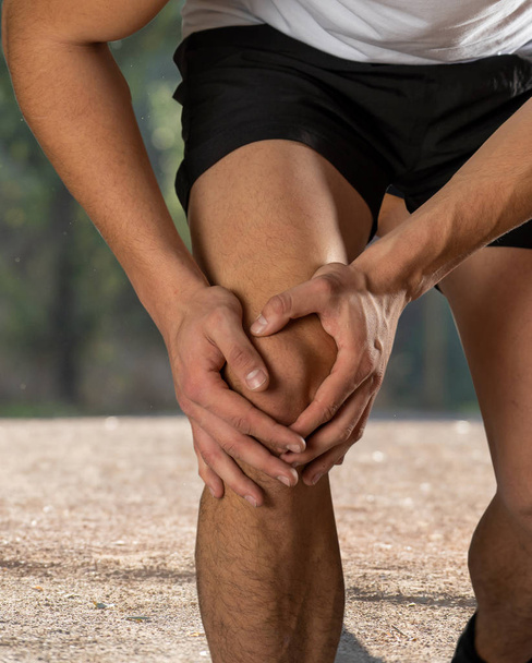 Young fit man holding knee with hands in pain after suffering muscle injury broken knee pain sprain or cramp during outdoors running. In Body pain and sport training injury and body health care. - Fotoğraf, Görsel
