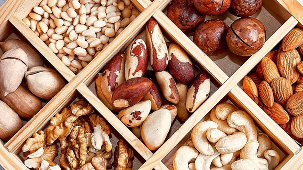 pecans, hazelnuts, almonds, pine nuts, brazil nut, cashews in a wooden box on blue background, top view, flat lay - Fotó, kép