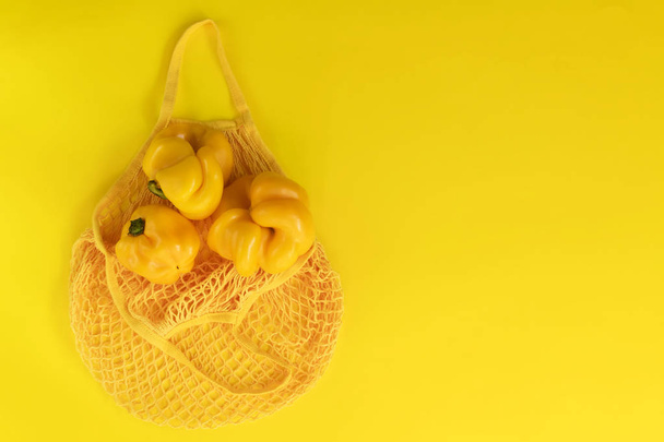 Жовтий струнний мішок з жовтим свіжим перцем на жовтому тлі. Екологічні біологічні продукти, потворні натуральні продукти харчування, здорові, дієтичні та вегетаріанські продукти
 - Фото, зображення