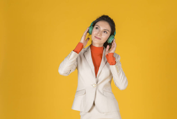 young woman listening to music with headphones and looking up on yellow background - Foto, Imagem
