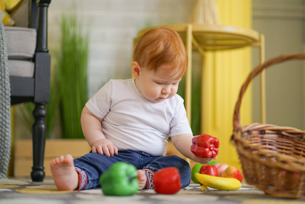 mollig kind met rood haar speelt met groenten - Foto, afbeelding