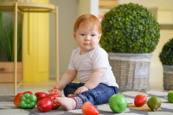 gordito niño con pelo rojo juega con verduras
 - Foto, imagen
