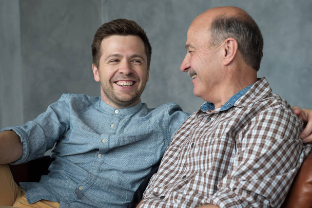 Lächelnder Senior-Vater sitzt auf Couch-Talk-Chat mit Millennial-Sohn verbringen Zeit zu Hause zusammen - Foto, Bild