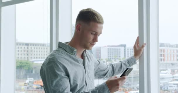 Side view close up of a young Caucasian creative businessman using a smartphone and looking out of the window in a modern office - Filmagem, Vídeo