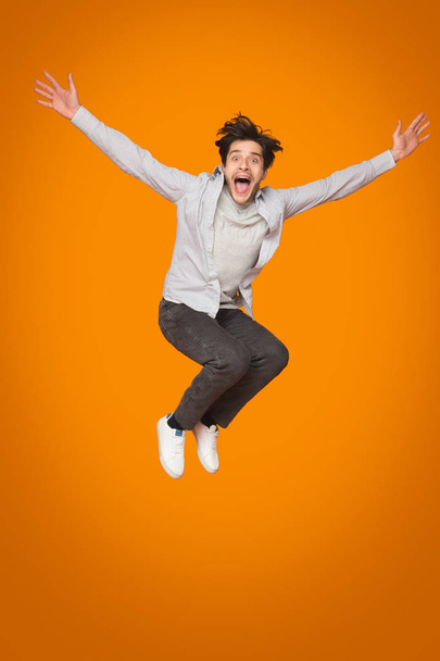 Τρελός πηδάει με ανυψά χέρια πάνω από πορτοκαλί φόντο - Φωτογραφία, εικόνα