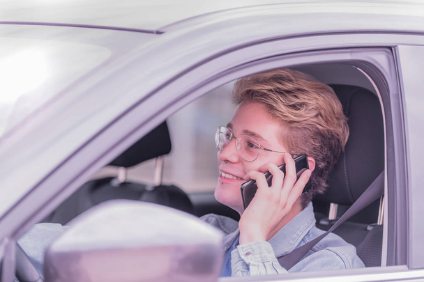 Sarışın çocuk bir arabada oturan ve düz ileriye bakıyor ve o telefonda konuşurken gülümseyerek. - Fotoğraf, Görsel