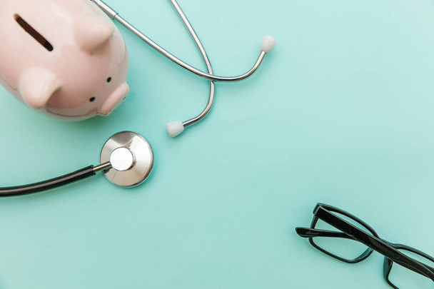 Lékařská lékařka zařízení stetoskop nebo fonendoskop prasátko z bankovních brýlí izolované na módní pastelové modré pozadí - Fotografie, Obrázek