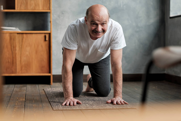 Homme hispanique senior pratique le yoga asana marjariasana ou pose chat-vache à la maison
. - Photo, image