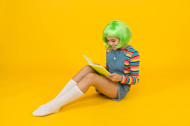 Geek girl reading comics magazine. Anime comics. Comics store. Anime fan. Cheerful kid in bright colorful wig. Cosplay party concept. Happy childhood concept. Hobby and interest. Reading literature - Photo, image