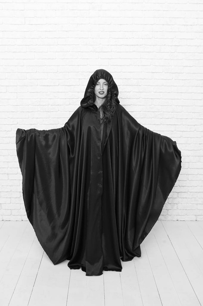 Death in black cloak symbol. Vampire in cloak sexy devil girl. Woman tempting vampire demon. Girl covered with cloak. Devil concept. Halloween masquerade. Halloween party. Damn pretty woman devil - Foto, imagen