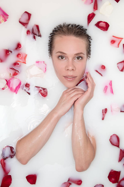 Portrait of a beautiful blonde girl in milk with rose petals in  - Photo, Image