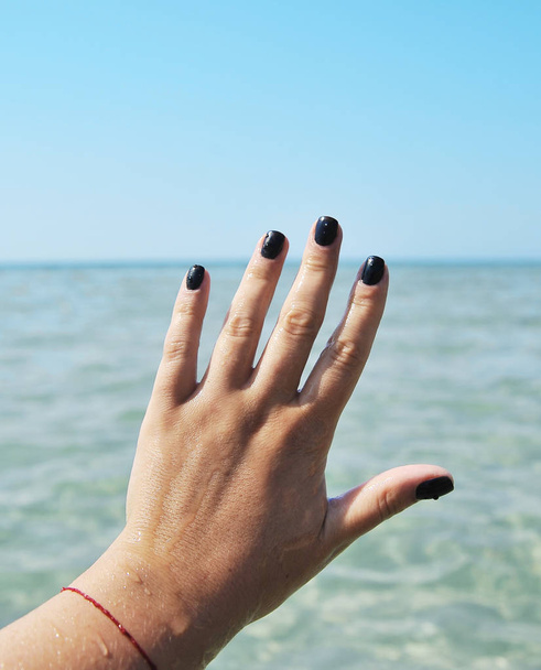 weibliche Hand mit schwarzen Nägeln auf Himmelshintergrund. - Foto, Bild
