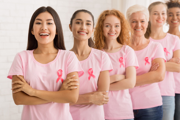 Frauen in Brustkrebs-T-Shirts stehen neben weißer Wand - Foto, Bild