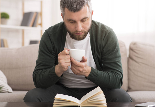 Parrakas mies juo kahvia lukiessaan kirjaa
 - Valokuva, kuva