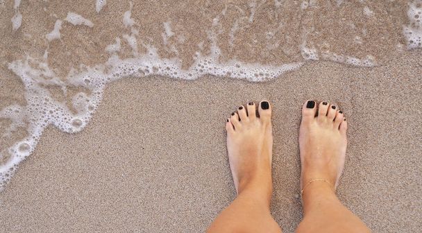 Piernas femeninas de pie sobre arena
. - Foto, Imagen
