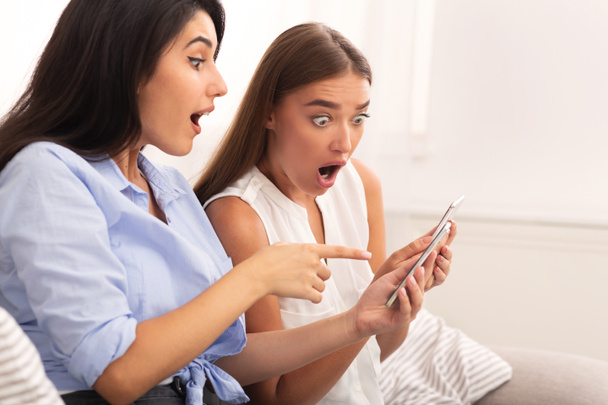 Two Amazed Girls Reading News Via Smartphone On Sofa Indoor - Photo, Image