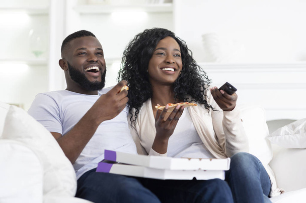 Güzel siyah çift pizza paylaşımı ve evde tv izlerken - Fotoğraf, Görsel