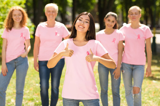 Mädchen gestikuliert mit erhobenem Daumen vor Brustkrebs-Freiwilligengruppe im Freien - Foto, Bild