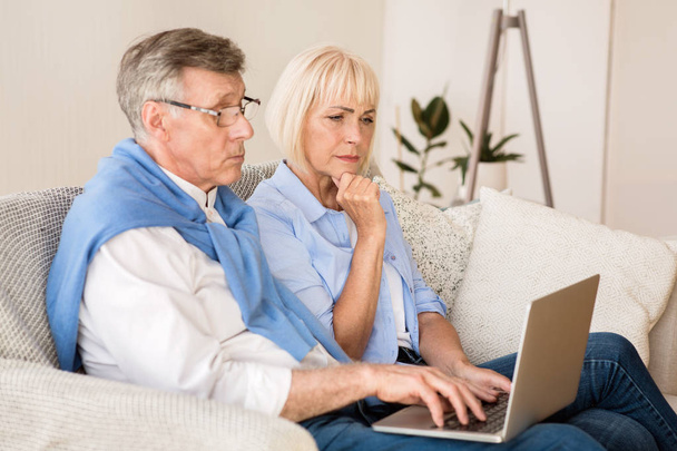 Senior paar lezen nieuws op laptop thuis - Foto, afbeelding
