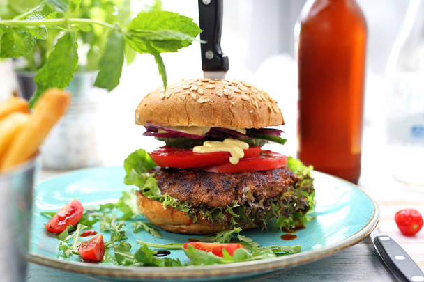 Izgara sığır püresi, domates, salatalık, marul ve sos ile klasik ev yapımı burger bir plaka üzerinde hizmet. - Fotoğraf, Görsel