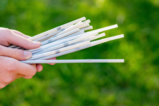 Hand holding white plastic straws on green grass background. Plastic pollution, environmental waste. Say no to plastic - Photo, Image