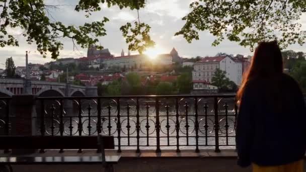 kaunis näkymä rantakadulta Vltava joen auringonlaskun kattojen taloja. Makea tyttö tulee ylös aidan katsomaan tätä viehättävä näkymä, Praha, Tsekin tasavalta
 - Materiaali, video