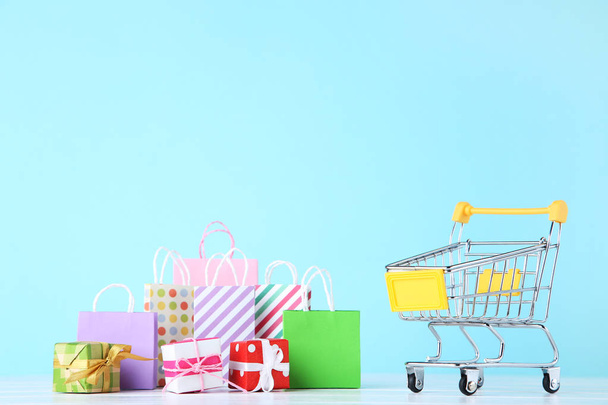 Small cart with gift boxes and shopping bags on blue background - Zdjęcie, obraz
