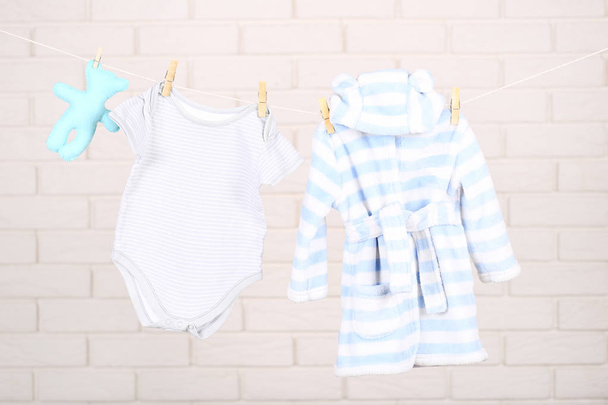 Baby clothes with soft toy hanging on brick wall background - Photo, image