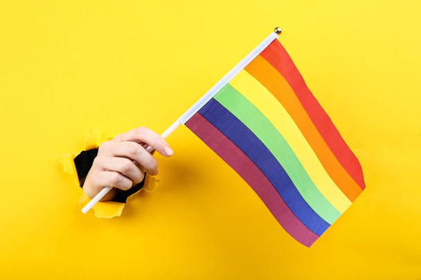 Hand holding rainbow flag from yellow torn paper - Zdjęcie, obraz