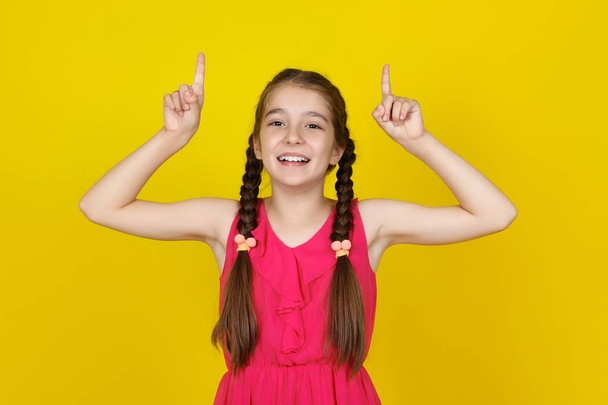 Beautiful young girl in pink dress showing fingers up on yellow  - Foto, Imagem