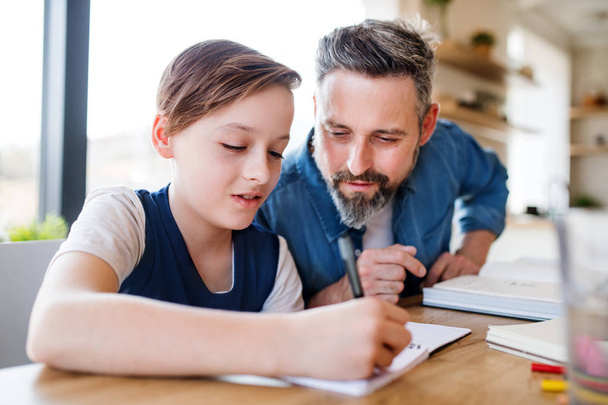 Mature father with small son sitting at table indoors, doing homework. - Photo, image