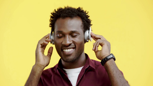dromerig Afrikaans amerikaanse man luisteren muziek in hoofdtelefoon geïsoleerd op geel - Video
