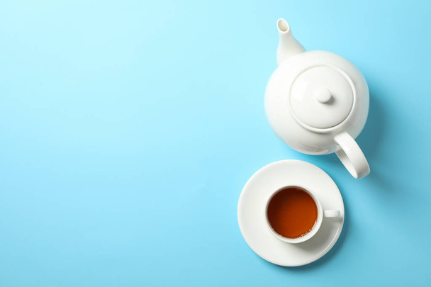 Cup of tea and teapot on blue background, space for text - Foto, afbeelding