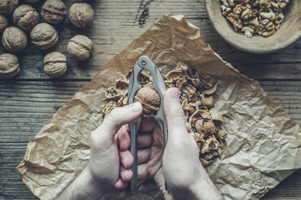 Man squeezes walnuts over wooden table - Photo, Image