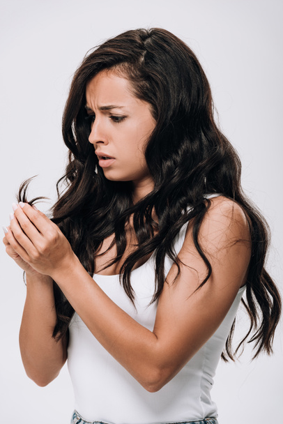 засмучена брюнетка красива жінка дивиться на пошкоджене волосся ізольовано на сірому
 - Фото, зображення