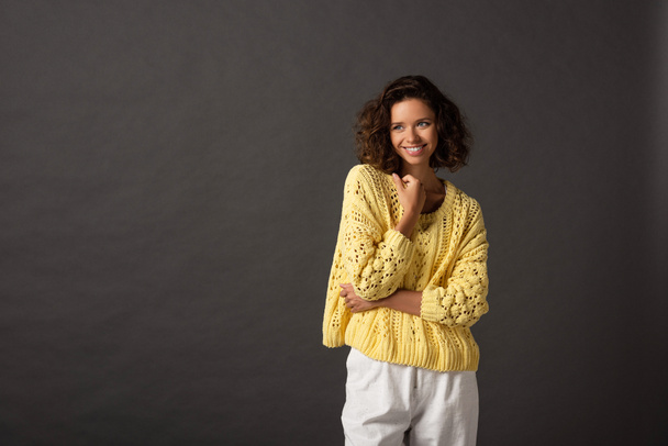 smiling curly woman in yellow knitted sweater looking away on black background - Fotografie, Obrázek