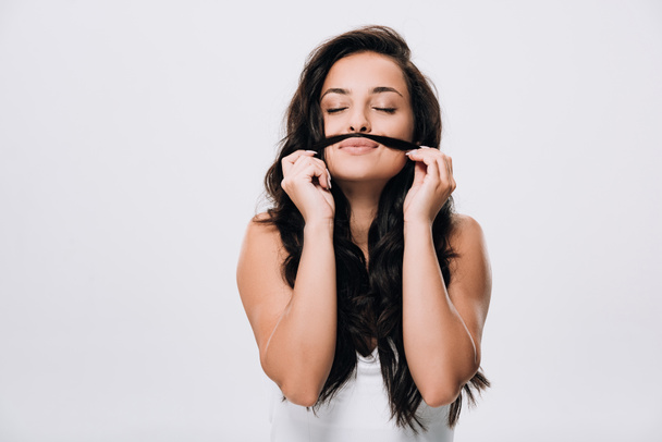 brunette beautiful woman with closed eyes making fake mustache from long healthy hair isolated on grey - Photo, Image